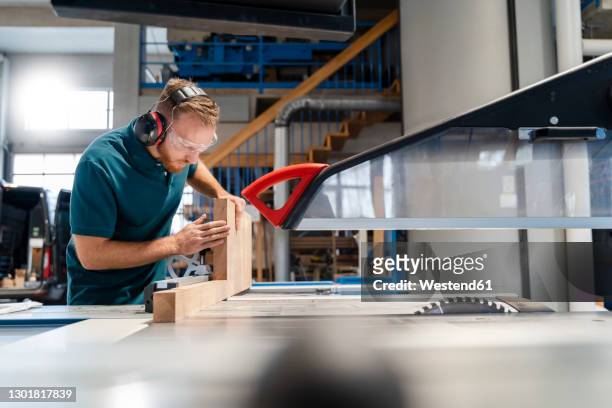 carpenter cutting plank on circular saw in production hall - elektrosäge stock-fotos und bilder