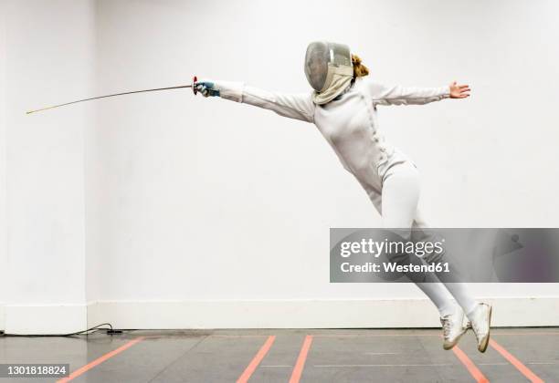 womanin fencing outfit practicing at gym - fechten stockfoto's en -beelden