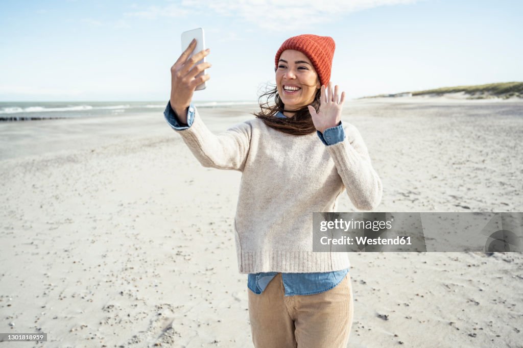 Portrait of woman wearing knit hat talking on smart phone at beach