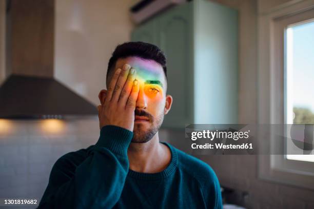 rainbow light hitting face of young man covering one eye with hand - colour spectrum stock-fotos und bilder