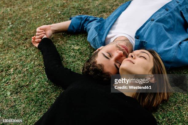 smiling couple lying on lawn - joue contre joue photos et images de collection