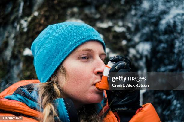 active female dressed in cold winter clothing uses asthma inhaler while climbing a mountain - inhaler stock pictures, royalty-free photos & images
