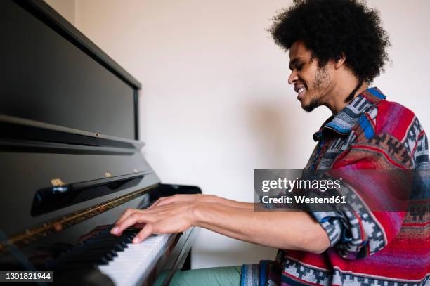 smiling male musician practicing on piano in living room - pianist stock-fotos und bilder