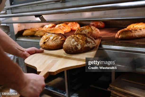 male chef with pizza peel removing baked bread from oven at bakery - bread fotografías e imágenes de stock