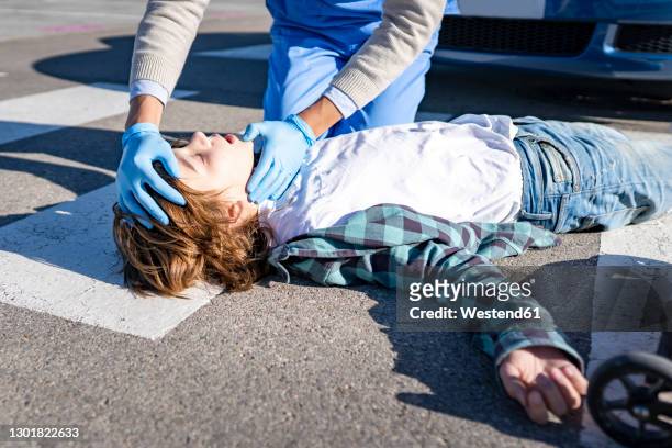 doctor checking unconscious boy lying on road after car accident - victim stock-fotos und bilder