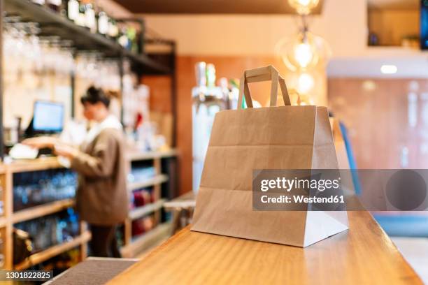 take out food kept in brown paper bag on bar counter during pandemic - paper bag stock pictures, royalty-free photos & images