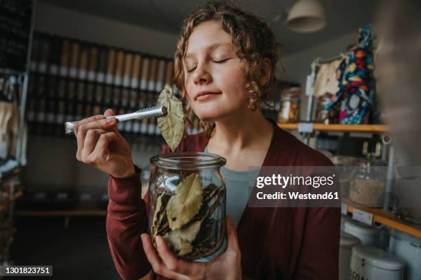 female clerk with eyes closed smelling bay leaf while working in zero waste shop - lorbeer stock-fotos und bilder