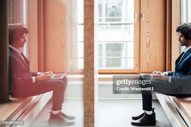 businessman using laptop with reflection of himself on glass at workplace - glass reflection in office stock-fotos und bilder