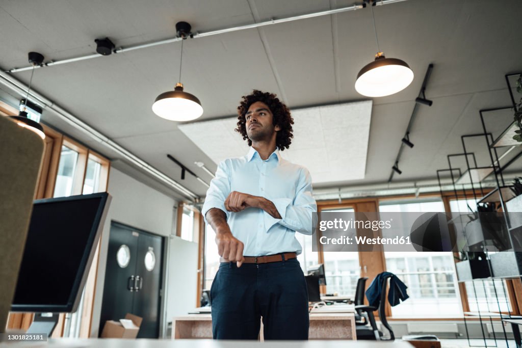 Confident young male professional rolling up sleeves in office