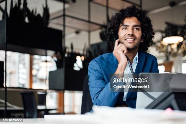 smiling businessman talking on telephone while sitting with laptop at office - festnetztelefon stock-fotos und bilder