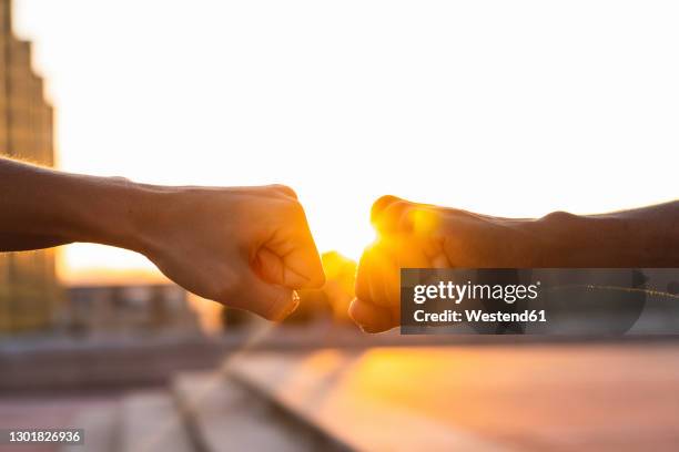 hands of friends giving fist bump to each other against clear sky during sunset - fist bump photos et images de collection