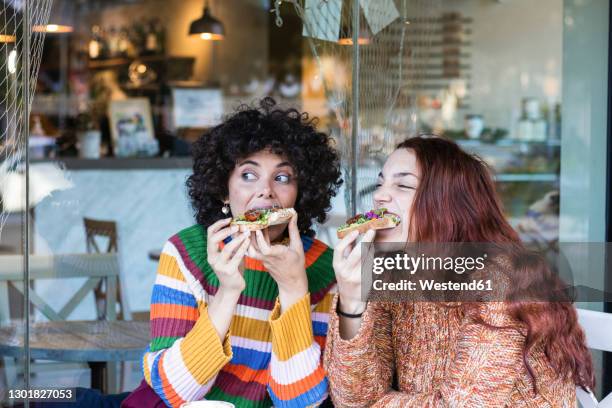 young woman having breakfast with friend while sitting at restaurant - eating bread stockfoto's en -beelden