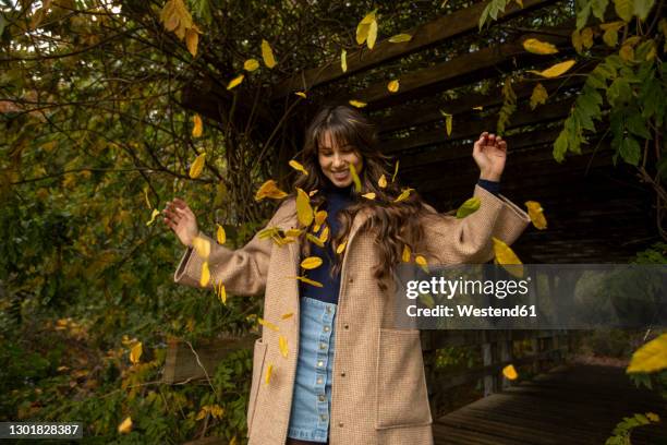 happy woman with arms raised standing in falling leafs at public park during autumn - denim skirt stock pictures, royalty-free photos & images