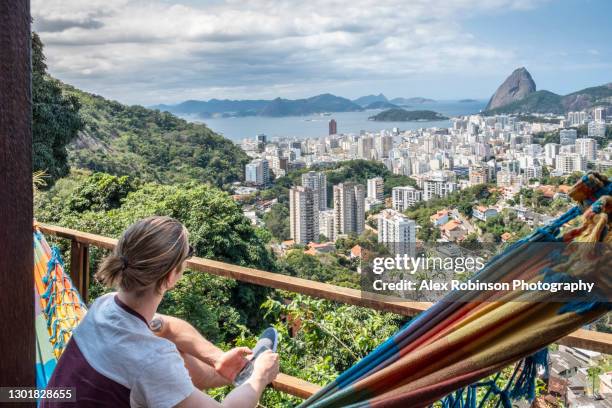 a young man sitting in a hammock in an vacation rental company house or hostel looking at the rio de janeiro skyline with a smart phone - sugar loaf bildbanksfoton och bilder