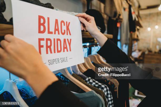 de verkoopster bevestigt een "zwarte vrijdag" teken in haar winkel - black friday shoppers stockfoto's en -beelden