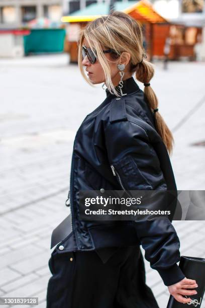 Influencer Gitta Banko wearing a low bubble ponytail hairstyle, a black bomber jacket by Saint Laurent, silver crystal heart 'YSL' earrings by Saint...
