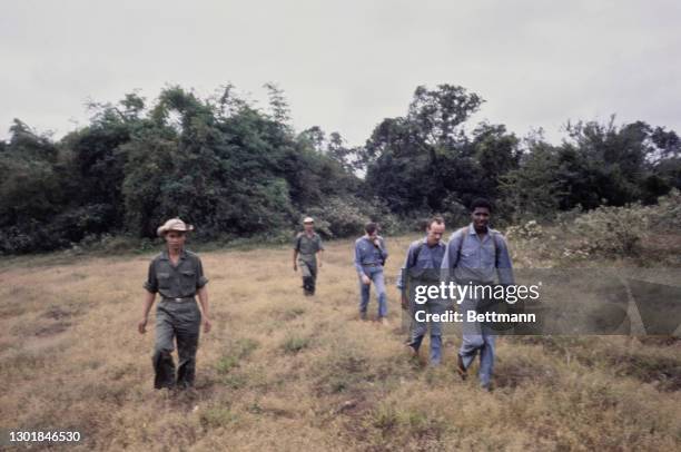 United States prisoners of war James Brigham, Thomas Jones and Donald Smith, each wearing blue trousers and blue shirts, walking in a line through...