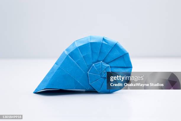 blue origami snail shell at white background - origami stockfoto's en -beelden