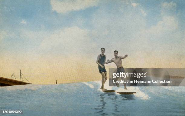 Souvenir postcard shows two men surfing side-by-side on a small one or two foot wave, circa 1908.