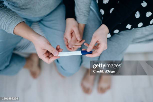 overhead view of an affectionate young asian couple sitting on the bed, holding hands and holding a positive pregnancy test together. it's finally happening. the long-awaited news. life events, fertility and family concept - screening of netflixs to all the boys ive loved before arrivals stockfoto's en -beelden