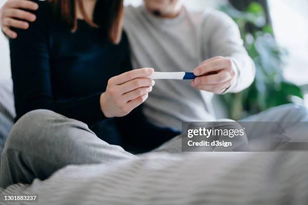 cropped shot of an affectionate young asian couple sitting on the bed holding a pregnancy test together, waiting for the result of the test. life events, fertility and family concept - pelvic exam fotografías e imágenes de stock