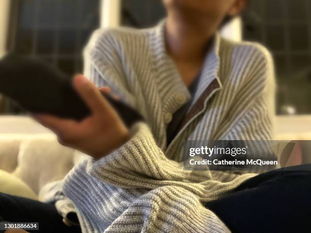 african-american woman holds remote control while watching television - cashmere jumper stock pictures, royalty-free photos & images