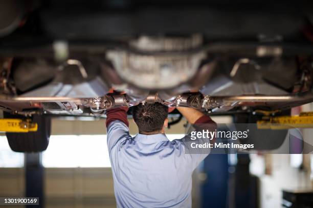 mechanic in a repair shop works on the underside of a car up on a lift - fahrgestell stock-fotos und bilder