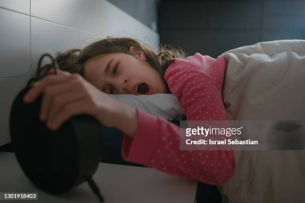 closeup of a girl yawning with her eyes closed as she is turning off her alarm clock to go to school. - bedside table kid asleep stock pictures, royalty-free photos & images