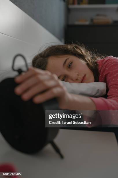 close-up of a girl with her eyes closed while she is turning off her alarm clock to go to school. - bedside table kid asleep stock pictures, royalty-free photos & images