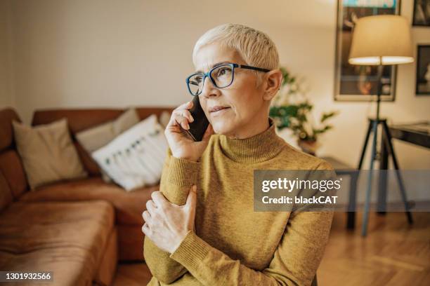美しい先輩女性がリビングルームで電話で話している - using phone ストックフォトと画像