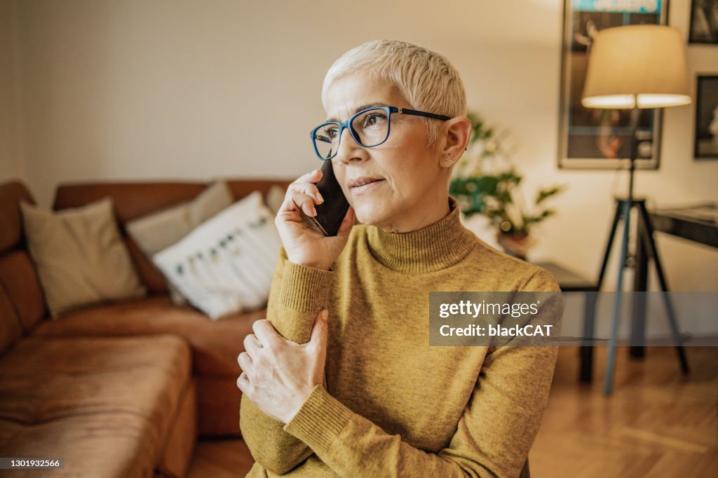 Beautiful senior woman is talking on the phone in the living room