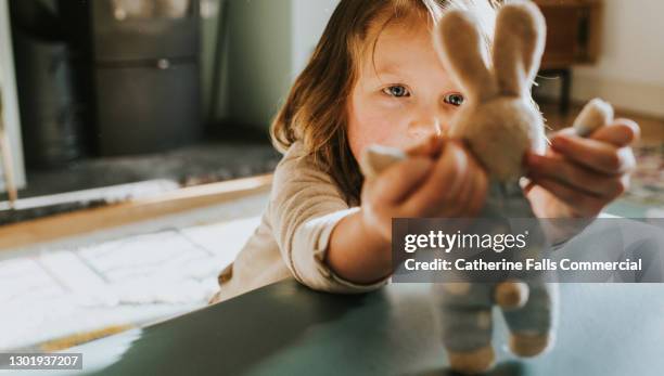 child holds and studies a small toy bunny - toy animal stock-fotos und bilder