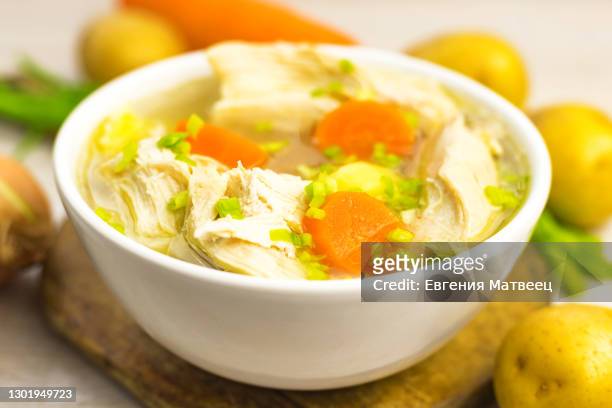 chicken soup stew broth and vegetables in white bowl on old rustic wooden cutting board - chicken stew stock pictures, royalty-free photos & images