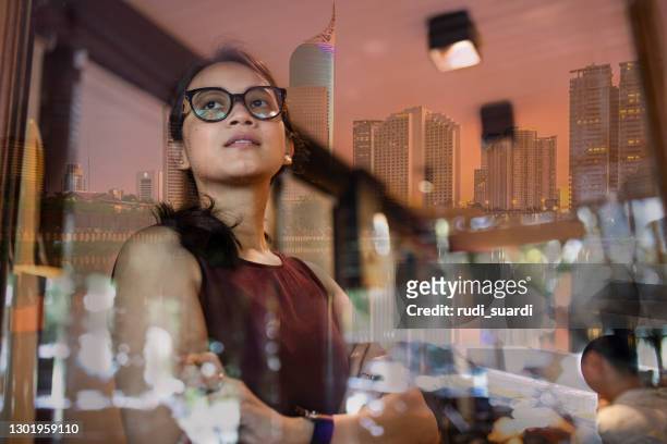 asian woman inside a office with jakarta cityscape  reflection in window - jakarta stock pictures, royalty-free photos & images