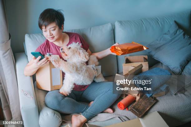 asian chinese mid adult woman happily unpacking opening all packages received all her parcel from online shopping with all her purchased delivered in living room sofa - shopaholic stock pictures, royalty-free photos & images