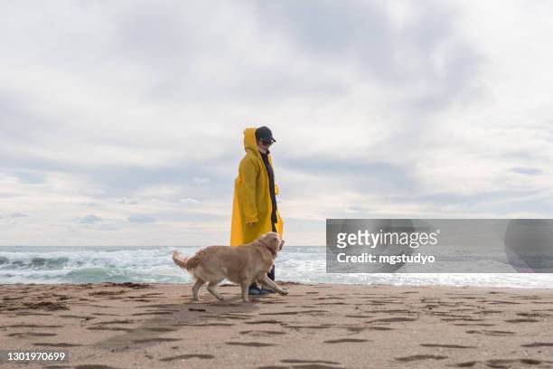 frau und ihr hund zu fuß am strand. - raincoat stock-fotos und bilder
