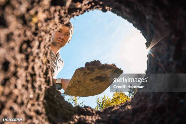 young handsome man digs a deep hole in the garden for planting plants and trees. gardening and farming, human work with soil - graben stock-fotos und bilder