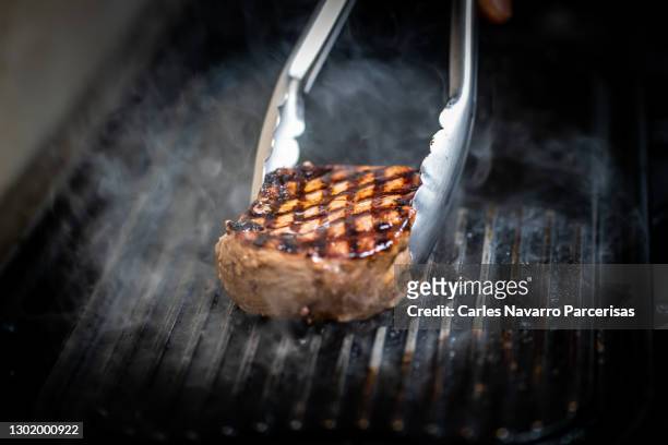detail of tongs grabbing a fillet of meat on the grill. costa rica gastronomy - grillzange stock-fotos und bilder