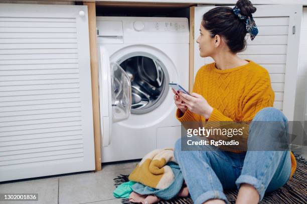 young woman using a mobile app to adjust her smart washing machine - máquina de lavar roupa imagens e fotografias de stock