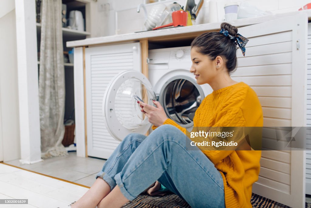 Young woman using a smart system to turn on her laundry machine