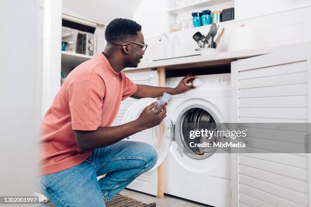 african american man watching a tutorial for handling a washing machine - afro man washing stock pictures, royalty-free photos & images