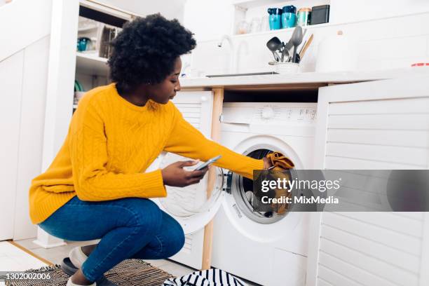 african american woman checking an online tutorial before turning on her washing machine - laundry woman stock pictures, royalty-free photos & images