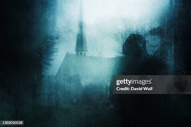 a spooky hooded figure, back to camera. looking at a church with tower. in a graveyard on a winters day. with a grunge, abstract edit. - spooky graveyard stock pictures, royalty-free photos & images