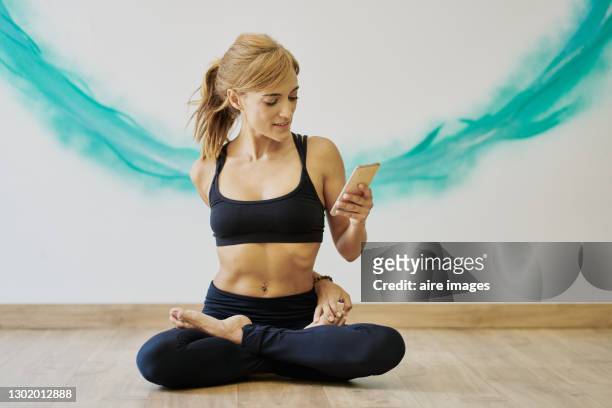 woman using mobile phone while stretching before a yoga class. - cell and body stock-fotos und bilder