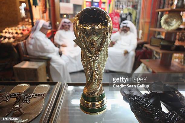 Arab men sit at a shoemaker's stall with a replica of the FIFA World Cup trophy in the Souq Waqif traditional market on October 24, 2011 in Doha,...