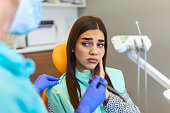 Young woman holding cheek in chair at dentist, having toothache. Shot of a young woman suffering from toothache while sitting in the dentist