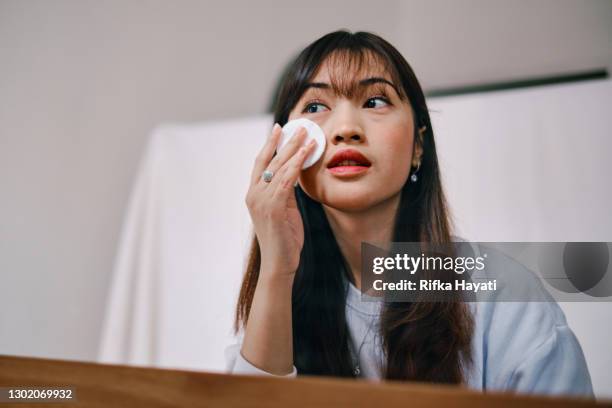 belle femme asiatique enlevant l’application de maquillage devant le miroir - démaquillant photos et images de collection