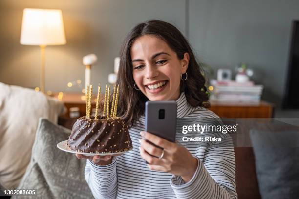 young woman holding a birthday cake and talking on a video call - zoom birthday stock pictures, royalty-free photos & images