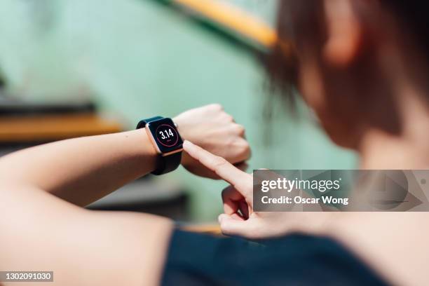 over the shoulder view of young active woman using exercise tracking app on smart-watch to monitor her training progress after running - ウェアラブルコンピュータ ストックフォトと画像