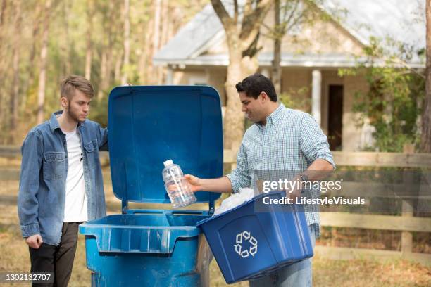 mid-adult latin descent and young caucasian men put recycle trach in bin. - bin stock pictures, royalty-free photos & images